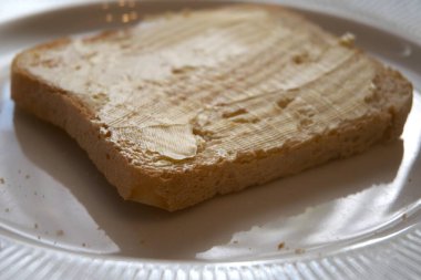 Beyaz tabakta margarin ile yayılmış kızarmış ekmek diliminin yakın görüntüsü..