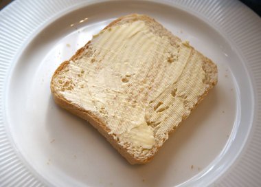 Beyaz tabakta margarin ile yayılmış kızarmış ekmek diliminin yakın görüntüsü..