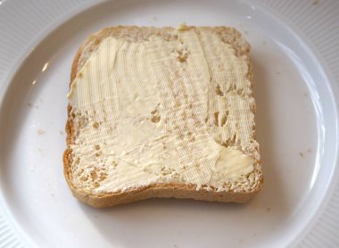 Beyaz tabakta margarin ile yayılmış kızarmış ekmek diliminin yakın görüntüsü..