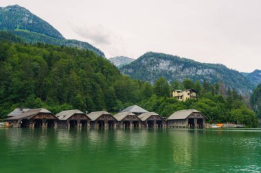 Kaliteli ahşap kayıkhaneler, sık ağaçlarla çevrili sakin, yeşil sular ve bulutlu bir gökyüzünün altında yükselen dağlar, doğada sakin bir atmosfer yaratıyor. Konigssee Gölü Bavyera Alman Alpleri