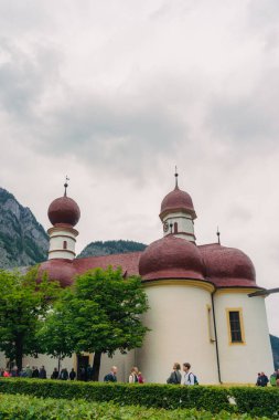 Görkemli dağlarla çevrili tarihi bir kilisenin yer aldığı büyüleyici bir göl köyü manzarası. Turistler, Konigsse Gölü 'nün sakin atmosferi ve güzel mimarisinin keyfini çıkarıyorlar.