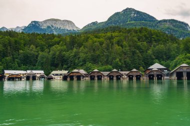 Kaliteli ahşap kayıkhaneler, sık ağaçlarla çevrili sakin, yeşil sular ve bulutlu bir gökyüzünün altında yükselen dağlar, doğada sakin bir atmosfer yaratıyor. Konigssee Gölü Bavyera Alman Alpleri
