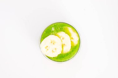 Beyaz zemin üzerinde muz dilimleriyle servis edilen yeşil smoothie tropikal meyve soslu sağlıklı detoks içeceği. Yüksek kalite fotoğraf