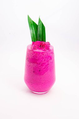 Şeffaf bardakta servis edilen canlı pembe smoothie beyaz arka plan ejderha meyvesinde yeşil tropikal yaprak garnitürlü. Yüksek kalite fotoğraf