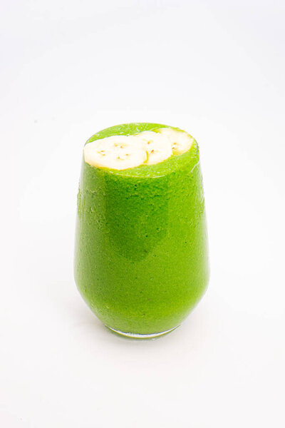 green smoothie with banana slices served in clear glass on white background healthy detox drink with tropical fruit topping. High quality photo