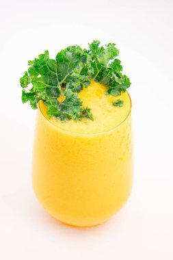 Sarı meyve suyu ya da şeffaf bardakta servis edilen ve temiz beyaz arka planda taze kıvırcık lahana ile süslenmiş meyve suyu. Yüksek kalite fotoğraf