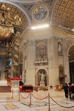 Gian Lorenzo Bernini 'nin tasarladığı Aziz Peters Bazilika Vatikan Şehri' ndeki Papalık Sunağı 'nın üzerindeki süslü Baldachin tepe örtüsünü büyük harflerin altında kırmızı çiçek sütunları ve Latince yazıtlarla süsledi.