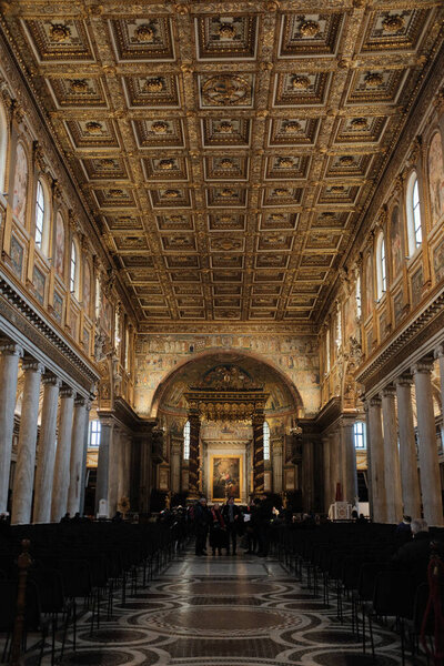 Украшенный золотой кессонный потолок и богато украшенный интерьер базилики Святой Марии-мажор в Риме с рядами скамеек мраморного пола и освещенным алтарем в дальнем конце. Высокое качество фото