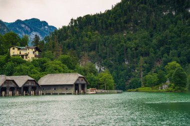 Kaliteli ahşap kayıkhaneler, sık ağaçlarla çevrili sakin, yeşil sular ve bulutlu bir gökyüzünün altında yükselen dağlar, doğada sakin bir atmosfer yaratıyor. Konigssee Gölü Bavyera Alman Alpleri