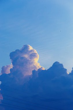 Yükselen kümülüs bulutları gün batımında açık mavi gökyüzüne karşı altın güneş ışığıyla parlarken dramatik doğal bulutlar ve atmosferik ışıkla birlikte. Yüksek kalite fotoğraf