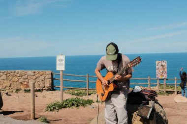 Güneşli bir günde Cabo da Roca Sintra Portekiz 'in deniz manzaralı sahili manzarasında akustik gitar çalan sokak müzisyeni. Yüksek kalite fotoğraf