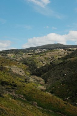 Bereketli yeşil tepeler ve engebeli arazi mavi gökyüzü ve dağılmış bulutlar Cabo da Roca Sintra Portekiz doğal manzarası manzaralı yürüyüş patikasından bitki örtüsü