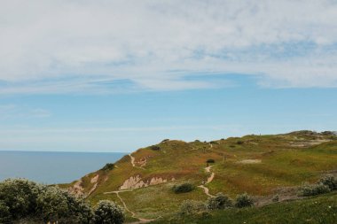 Cabo da Roca Sintra Portekiz 'deki manzaralı kıyı şeridi boyunca yürüyen yürüyüşçüler Atlantik Okyanusu' na bakan çimenli kayalıklarla Avrupa 'nın en batısındaki bulutlu gökyüzünün altında açık hava seyahatleri yapıyorlar. Yüksek