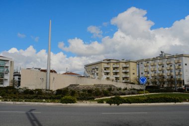 Mavi gökyüzü ve bulutların altındaki binaları çevreleyen Fatima Portugal yerleşim bölgesinde dikey beyaz sütunlu uzun modern anıt. Yüksek kalite fotoğraf