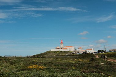 Bereketli yeşil tepeler ve engebeli arazi mavi gökyüzü ve dağılmış bulutlar Cabo da Roca Sintra Portekiz doğal manzarası manzaralı yürüyüş patikasından bitki örtüsü