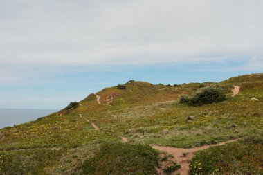 Cabo da Roca Sintra Portekiz 'deki manzaralı kıyı şeridi boyunca yürüyen yürüyüşçüler Atlantik Okyanusu' na bakan çimenli kayalıklarla Avrupa 'nın en batısındaki bulutlu gökyüzünün altında açık hava seyahatleri yapıyorlar. Yüksek
