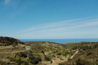 Sintra Portekiz 'deki Cabo da Roca deniz feneri manzaralı kıyı yolu Atlantik Okyanusu' na bakan doğal kayalıklardan geçen açık mavi gökyüzü altında.