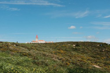 Bereketli yeşil tepeler ve engebeli arazi mavi gökyüzü ve dağılmış bulutlar Cabo da Roca Sintra Portekiz doğal manzarası manzaralı yürüyüş patikasından bitki örtüsü