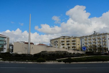 Mavi gökyüzü ve bulutların altındaki binaları çevreleyen Fatima Portugal yerleşim bölgesinde dikey beyaz sütunlu uzun modern anıt. Yüksek kalite fotoğraf