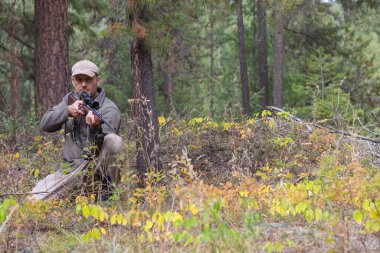Ormanda avlanmak. Avcı dizlerinin üstüne çöküp elinde tüfekle onu izliyor ve ateş etmeye hazır. Ön görünüm.