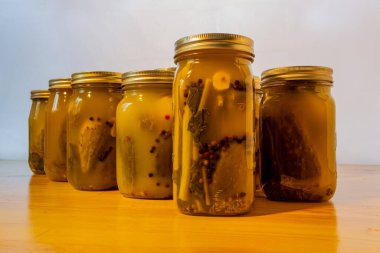 Glass jars filled with pickled cucumbers on a wooden table against a white background. clipart