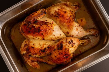 Güzel kavrulmuş bir yüzeyi olan, paslanmaz çelik kızartma tavasının içindeki sıvılarında dinlenen akromatik fırında pişirilmiş tavuk. Üst görünüm