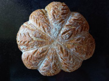 Bir İtalyan ekşi ekmeği balkabağı şeklinde, yukarıdan gelen narin ışık ve koyu taştan bir zemin. Ekmeğin desenleri ve un hamurunda kesikleri var. Rengi açık kahverengi ve beyaz..