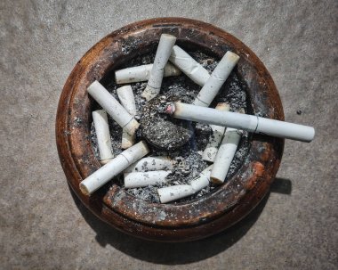 Beyaz bir sigaranın üst açısı ve sigara izmaritleri ahşap kül tablasında