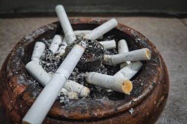 Beyaz sigaranın yakın plan portresi ve ahşap küllükte sigara izmaritleri.