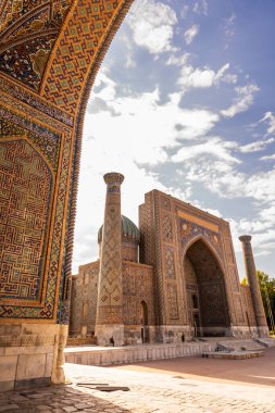 Bir Registan Meydanı medresesinin büyüleyici bir perspektifi diğerinin kemeriyle mükemmel çerçevelenmiş, karmaşık tasarımları ve tarihi cazibeyi vurguluyor..