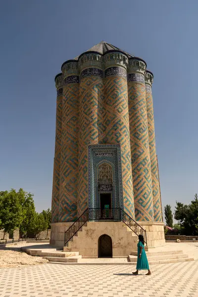 Azerbaycan 'ın Nakhchivan kentindeki tarihi Garabaghlar Anıtmezarının yanında bir kadın yürüyor. Parlak güneşli bir gün, bu antik şehrin karmaşık mimarisi ve sakin çevresini vurguluyor..