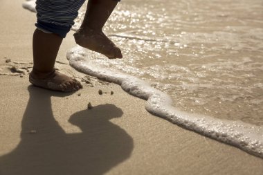 Close-up of a baby's tiny feet stepping into gentle waves on a sunny beach. The warm sand and glistening water capture the beauty of childhood moments. clipart