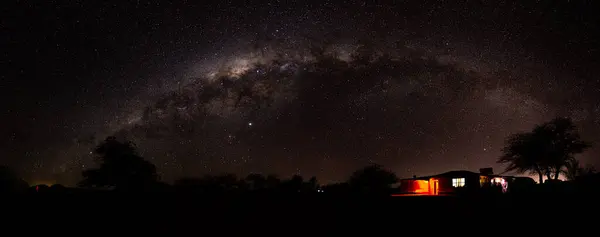 Atacama Çölü 'nden göz kamaştırıcı bir gece manzarası yıldızlarla dolu gökyüzünü ve Samanyolu' nun kavisini gösteriyor. Yerdeki küçük bir ev ve ağaç bu göksel manzaraya derinlik katar.