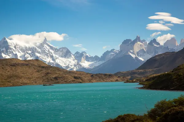 Torres del Paine Ulusal Parkı 'nda el değmemiş bir buzul gölü. Yükselen dağlar açık bir gökyüzünün altında dramatik bir zemin oluşturuyor. Nefes kesici bir Patagonya sahnesi.