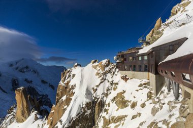 Güneşli bir kış gününde açık mavi gökyüzü ve karla kaplı arazisiyle Chamonix tepelerinin tepesine bakan güverteler..