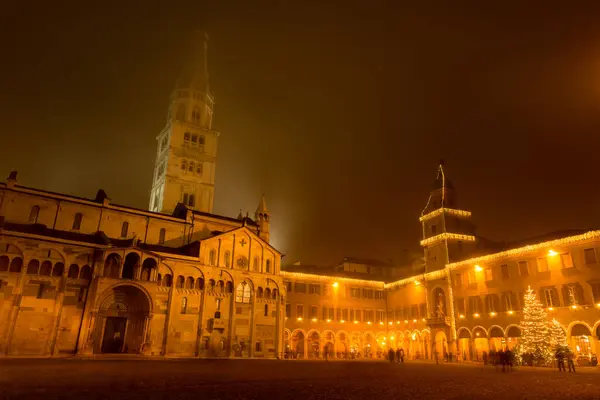Modena Meydanı sisli bir kış gecesinde Noel süslemeleri, bir Noel ağacı ve sisle kaplı bir katedral kulesi..