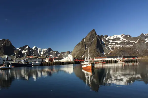 Lofoten balıkçı köyündeki Rorbu evleri ve tekneleri, sakin sularda yansıyan karla kaplı dağlarla.