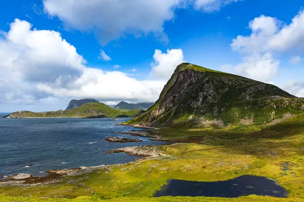 Norveç 'in Lofoten kentindeki dağlarla çevrili turkuaz yeşili fiyort suyu parçalı bulutlu bir günde. Ön planda küçük bir göl görünüyor.