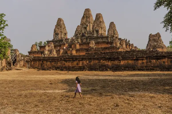 Arka planda görkemli bir yapısı olan küçük bir kız Pre Rup tapınağının yanında yürüyor. Turistler antik tapınak kompleksini keşfediyorlar.