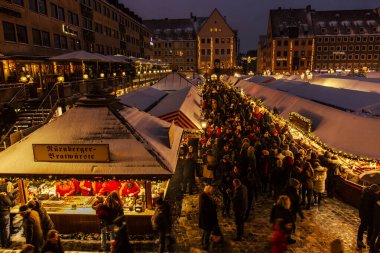 Magical night shot of Nuremberg Christmas Market. Snow covers shop roofs, and the market buzzes with shoppers under festive lights. clipart