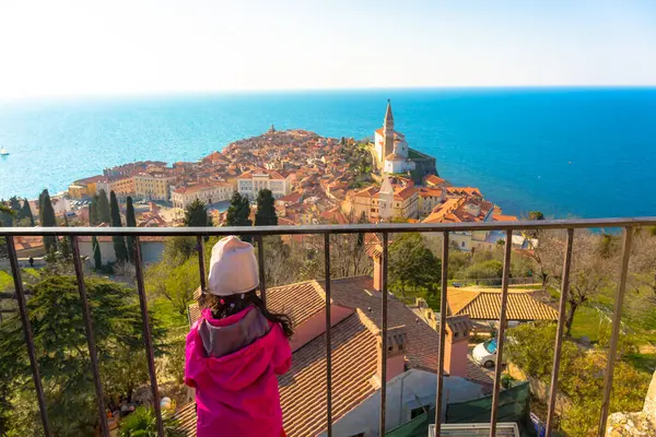 Küçük bir kız, güneşli bir günde Slovenya 'nın eski Piran kasabasının manzarasına hayran. Kızıl çatılar ve ötesinde mavi deniz çarpıcı bir manzara yaratır..