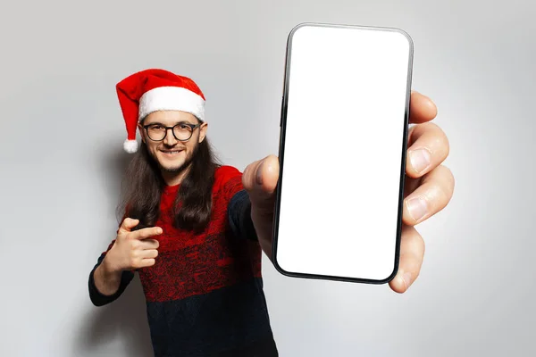 아무것도 스마트폰을 기기를 가리키며 크리스마스 스웨터와 모자를 배경에 스튜디오 — 스톡 사진