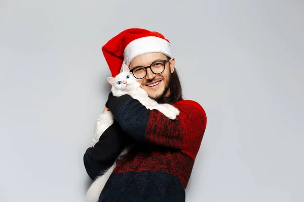 남성의 스튜디오 사진붉은 크리스마스 스웨터를 고양이를 껴안고 모자를 배경에 — 스톡 사진