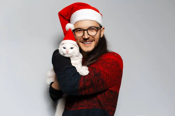 스튜디오 사진붉은 크리스마스 스웨터를 고양이를 껴안고 모자를 배경에 — 스톡 사진