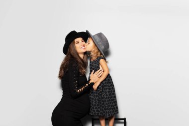 Genç mutlu hamile kadının stüdyo portresi, kızı beyaz arka planda annesini öpüyor. Siyah şapkalı..