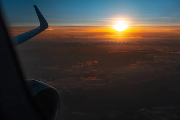 Scenic view of beautiful sunrise, cloudy sky and airplane wing with engine, through window of the aircraft during the flight. Copy space. Silhouette of airliner. Colourful yellow sunset above Cyprus.