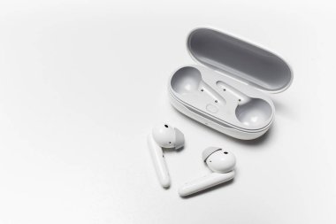 Close-up of modern wireless earphones lying near opened charging case on white background with copy space.