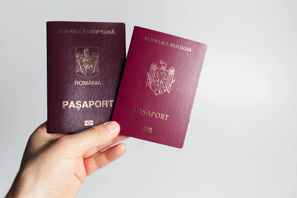 Close-up of male hand holding Romanian and Moldavian passports in hand on white background.