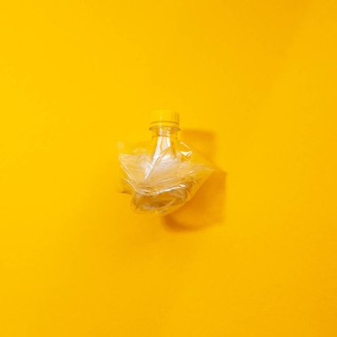 Sarı arka planda izole edilmiş buruşmuş plastik şişenin yakın çekimi.