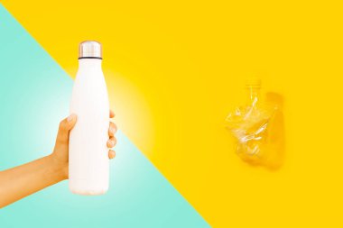 Çelik termik su şişesi, kadın eli maketi ve buruşmuş plastik şişe, sarı ve cyan renkli..